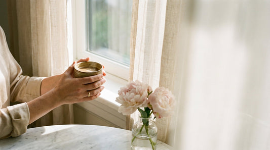 Woman's hands cradling a warm coffee cup by a sunlit window with pink peonies — Chica Bonita Coffee daily ritual moment